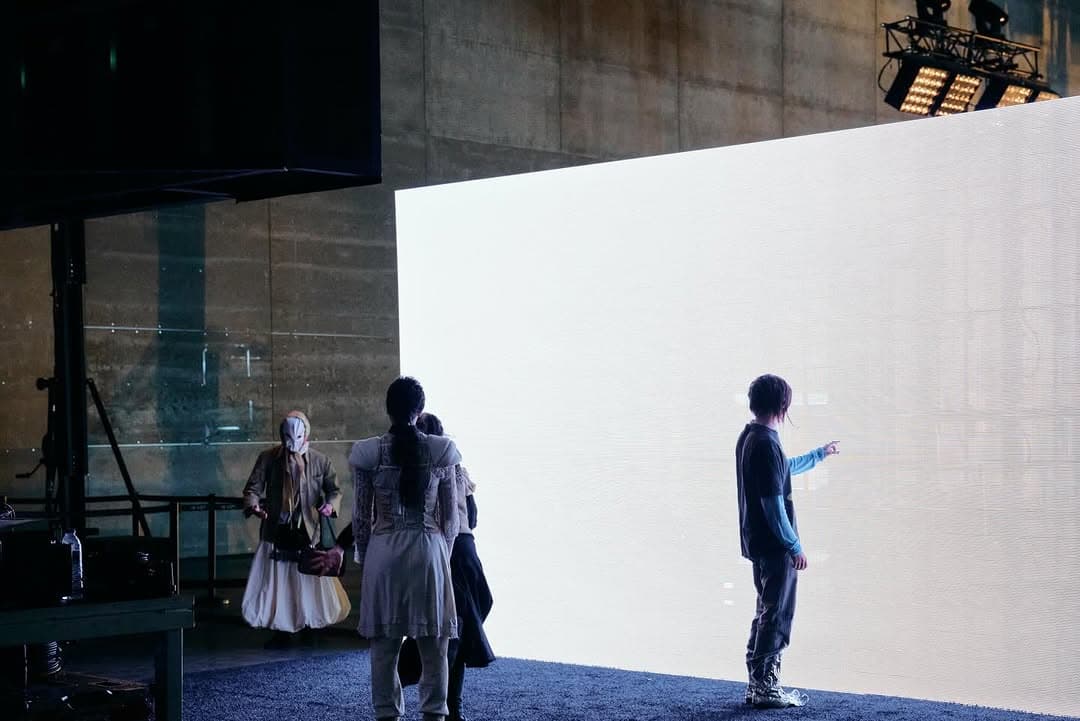 Visitors standing before a lit white wall in a dark hall