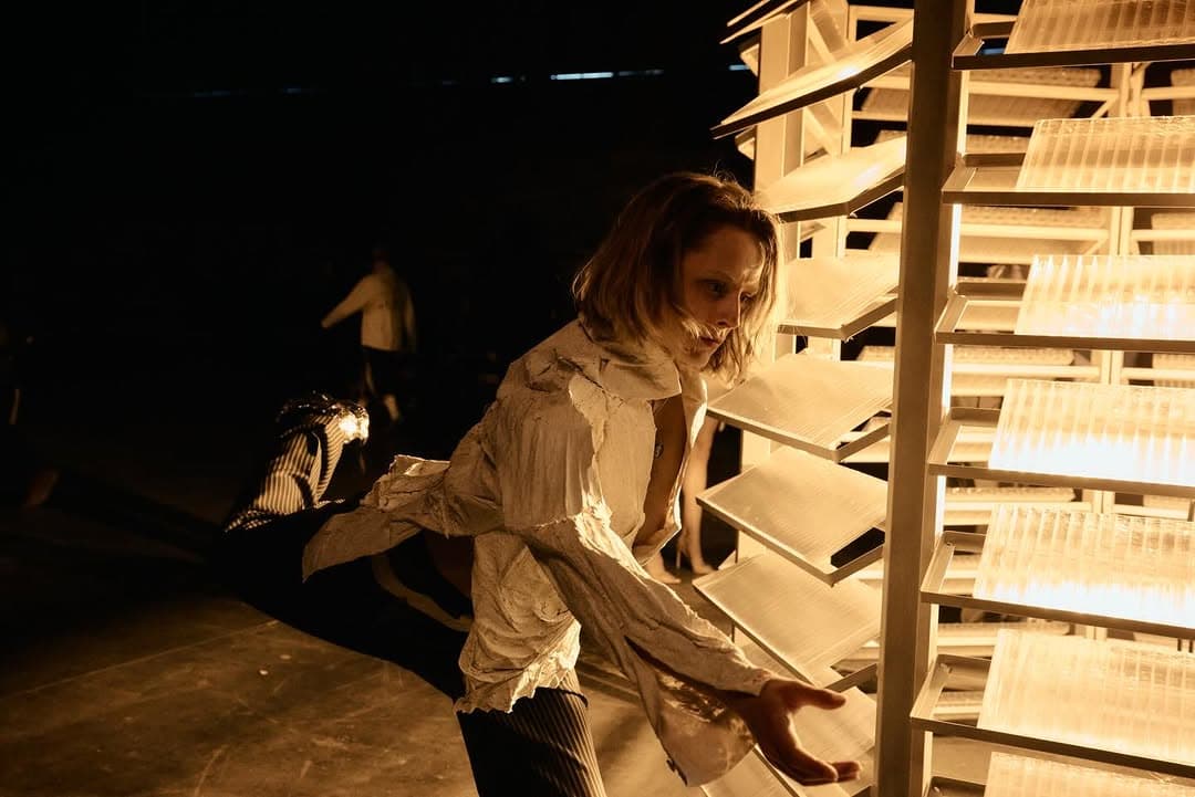 A woman in a pale shirt leaning into a lit wooden shelf
